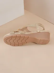 Detail view of the non-slip rubber sole and wedge heel of the golden sandal.