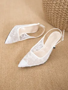 Close-up of elegant white mesh high heels with delicate floral lace and pointed toe.