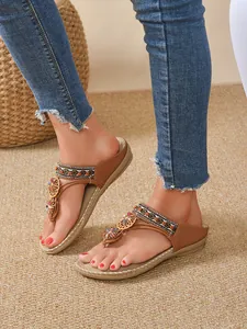 Close-up of bohemian flat sandals with rhinestone flower and ethnic woven strap on feet.