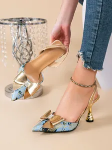 Detail van blauwe bloemenpumps met gouden strass-strik en een bewerkte hak.