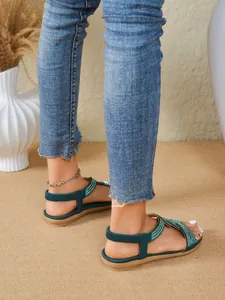 Detail view of ethnic style flat sandals with green rhinestone straps worn by a model.