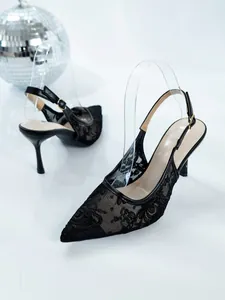 Close-up of black lace mesh pointed-toe high heels with slingback strap and party decor