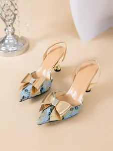 Detail van lichtblauwe pumps met puntige neus en een grote gouden strass strik decoratie.
