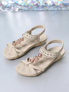 Close-up of beige Bohemian flat sandals with floral beading and metallic stud details.