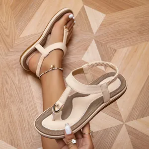 Close-up of beige Bohemian thong sandals with elastic ankle strap and gold hardware.