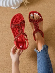Detailed view of red ethnic style flat sandals with rhinestone straps on model's feet.