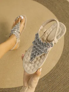 Close-up of beige flat thong sandals with intricate rhinestone leaf embellishments