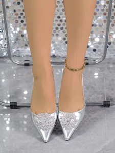 Detail view of silver pointed-toe stiletto pumps with sparkling rhinestone toe decoration.