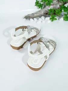 Close-up of white women's flat sandals with sparkling rhinestones and elastic heel strap