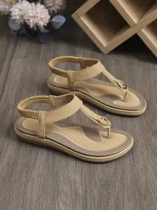 Detalle de sandalias planas bohemias con hebilla en T y correa elástica al talón.