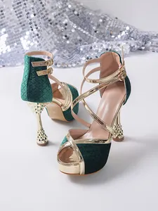 Close-up detail of emerald green velvet high heels with gold cross straps and wine glass heels.