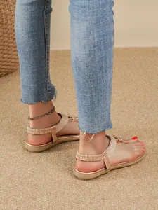 Close-up of Bohemian rhinestone flat sandals worn with denim jeans on a tan rug.