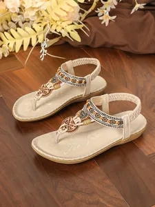 Detail view of beige Bohemian flat sandals with ethnic embroidery and rhinestones on wood.