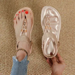 Elegant rose gold bohemian flat thong sandals with rhinestones on a textured mat.
