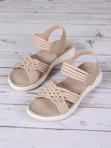 Primo piano di sandali bohémien beige con cinturini intrecciati su pavimento in legno