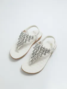 Detalle de sandalias planas blancas bohemias con exquisitos adornos de pedrería y cuentas