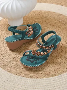 Close-up detail of teal bohemian wedge sandals with colorful beads and heart charms