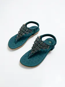 Primer plano de sandalias bohemias verde azulado con adornos de pedrería y cuentas finas