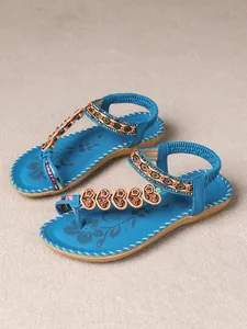 Detail of blue Bohemian flat sandals with beaded floral T-strap design on fabric background.