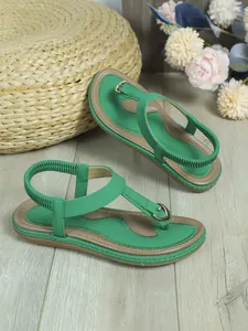 Detalle de sandalias planas verdes con tira en T y banda elástica en suelo de madera