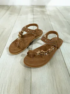 Bohemian brown flat sandals with rhinestone and bead details on light wood floor backdrop