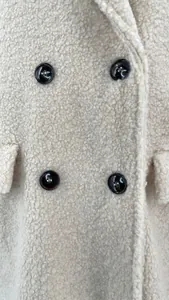 Detailed close-up of cream teddy fleece fabric and dark double-breasted buttons