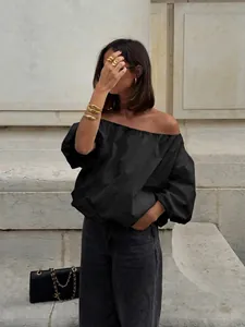 Detail shot of a chic black cotton off-shoulder blouse with puffy sleeves in a street setting.
