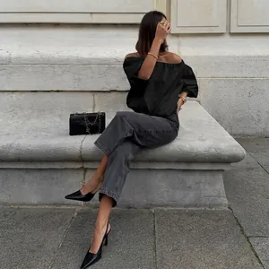Woman wearing a black off-the-shoulder puff sleeve top in a chic urban outdoor setting.