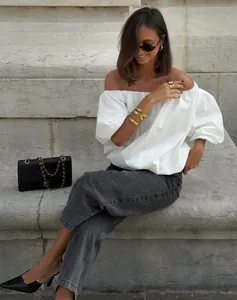 Chic white off-shoulder cotton blouse worn by model on stone steps in soft outdoor light