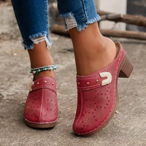 Close-up of red vintage carved chunky heel mules with floral patterns and studs.