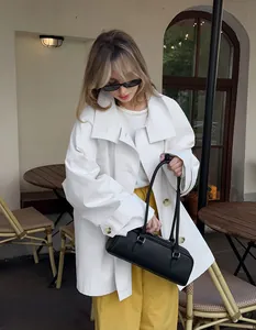 Stylish white mid-length oversized trench coat for women in an outdoor cafe setting.