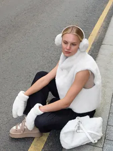 Model wearing a white faux fur vest, earmuffs, and mittens on a city street