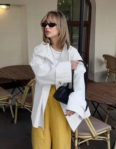 Close-up detail of a white oversized women's trench coat styled in a street cafe