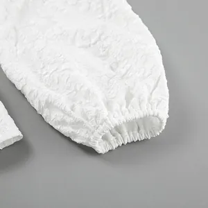 Dettaglio macro di manica a sbuffo in jacquard bianco a rilievo con polsino elastico.