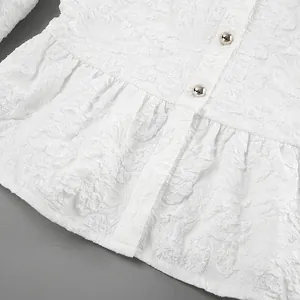 Dettaglio del tessuto jacquard bianco con bottoni dorati su una camicetta peplo vintage.