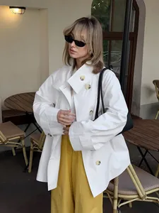 Detailed view of oversized white trench coat styled with yellow trousers in a cafe setting.