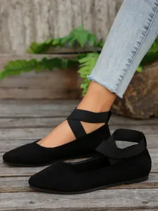 Primer plano de bailarinas negras de ante con punta afilada y tiras elásticas cruzadas.
