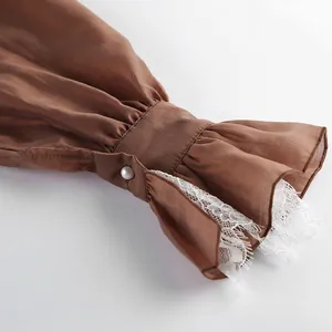 Primer plano del puño de camisa de tencel marrón con encaje blanco y botón de perla.