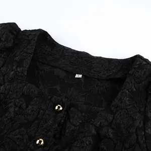 Dettaglio del tessuto jacquard nero e bottoni dorati su una camicetta con scollo quadrato.