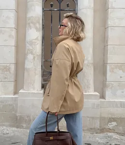 Vue latérale d'une femme portant un coupe-vent kaki cintré et un jean bleu.