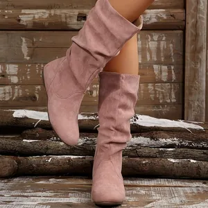 Detailed view of pink suede slouchy mid-calf boots with side zipper and rustic wood backdrop