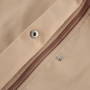 Gros plan d'un trench-coat kaki avec fermeture éclair et bouton-pression en métal.