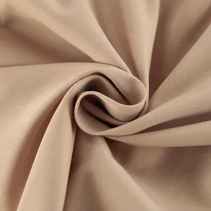 Gros plan du tissu beige d'un trench-coat montrant le tissage sergé et la texture lisse.