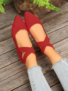 Primer plano de elegantes bailarinas de ante rojo con punta fina y correas elásticas cruzadas
