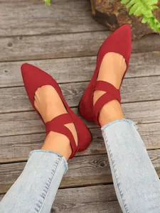 Bailarinas de ante rojo con punta fina y correas elásticas cruzadas sobre suelo rústico.