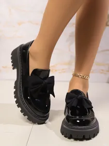 Nahaufnahme schwarzer Lackoberfläche und dekorativer Textilschleife an Plateau-Loafers.