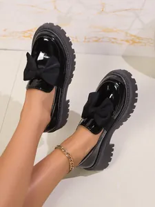 Detailansicht von schwarzen Lackleder-Loafers mit großer Schleife und dicker Plateausohle