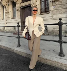 Model draagt een elegante beige blazer met V-hals, schoudervullingen en een getailleerde taille.