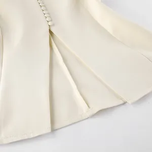 Detailopname van een crèmewitte blazer met kleine beklede knopen en fijne stiksels.