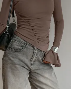 Detail eines taupefarbenen Langarm-T-Shirts mit geraffter Taille und silbernem Armreif.